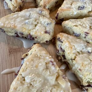 A wooden cutting board topped with scones covered in icing.