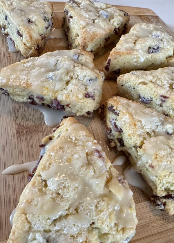 A wooden cutting board topped with scones covered in icing.