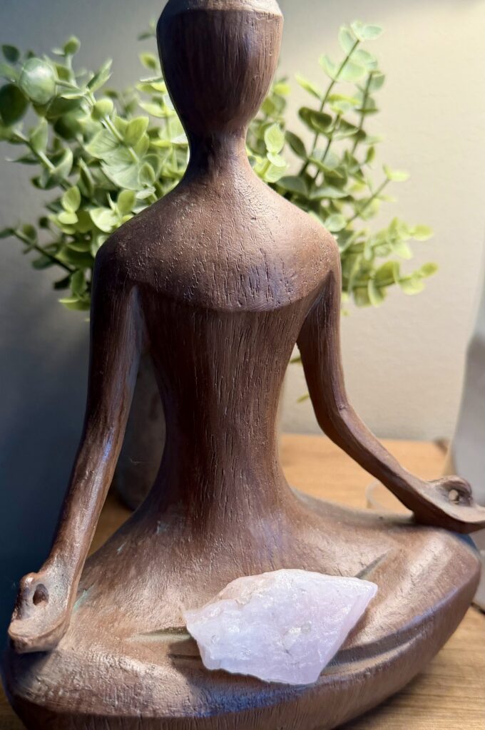 Wooden meditating figure with crystal, leafy background.