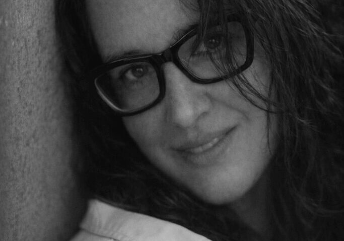 Woman with glasses, smiling in black and white.