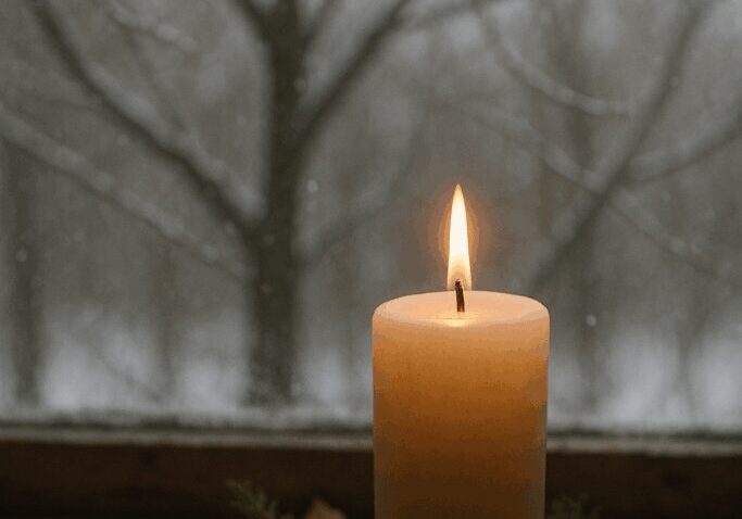Lit candle on snowy windowsill with branches.