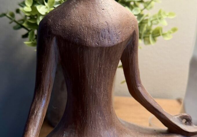 Wooden meditating figure with crystal, leafy background.