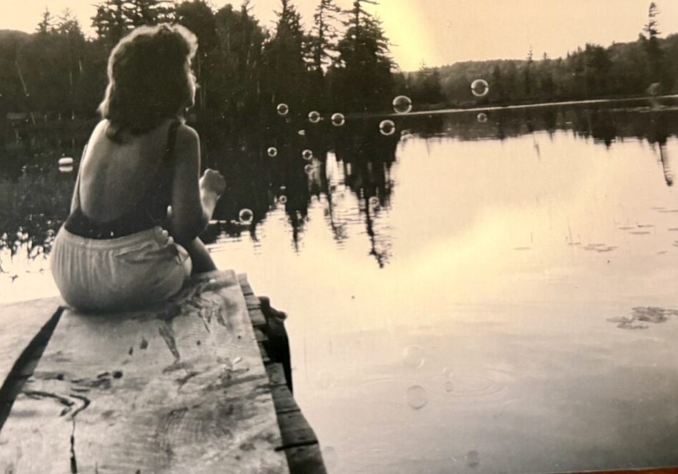 Woman sitting on dock blowing bubbles.